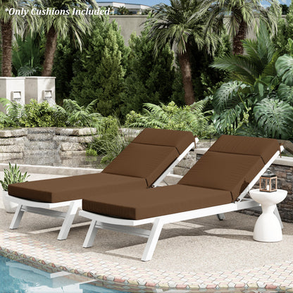 Two brown cushioned lounge chairs by a pool with palm trees and greenery in the background.