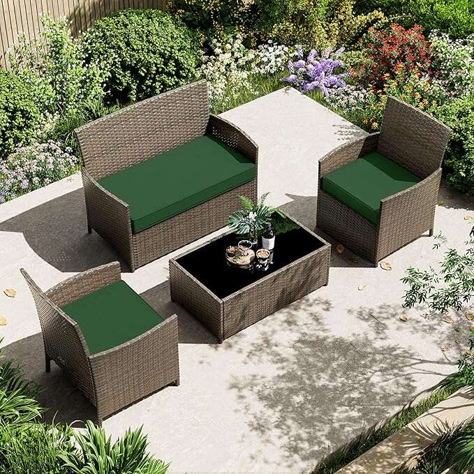 Outdoor patio set with rattan loveseat, two chairs with green cushions, and black glass coffee table
