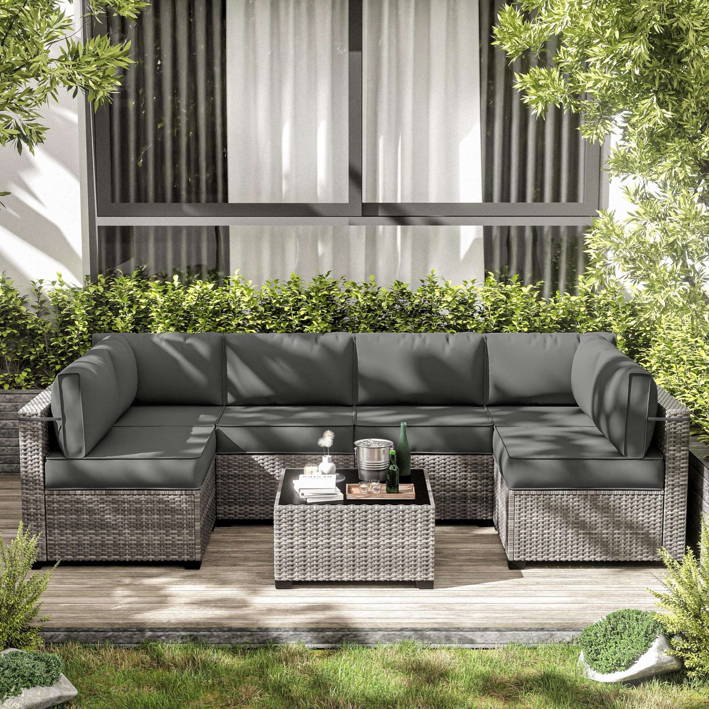Gray outdoor sectional sofa with cushions on a wooden deck, surrounded by greenery.
