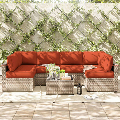 Outdoor patio furniture set with orange cushions against a stone wall with greenery.