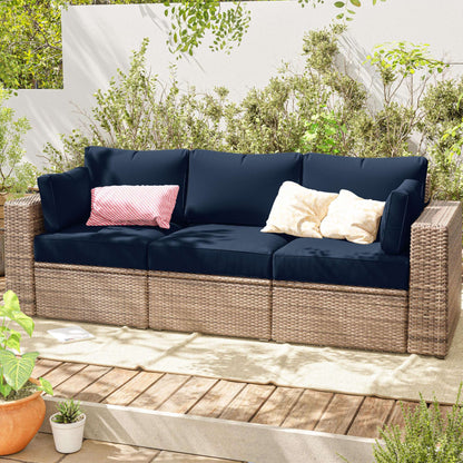 Outdoor sofa with navy cushions and decorative pillows on a wooden deck with greenery.