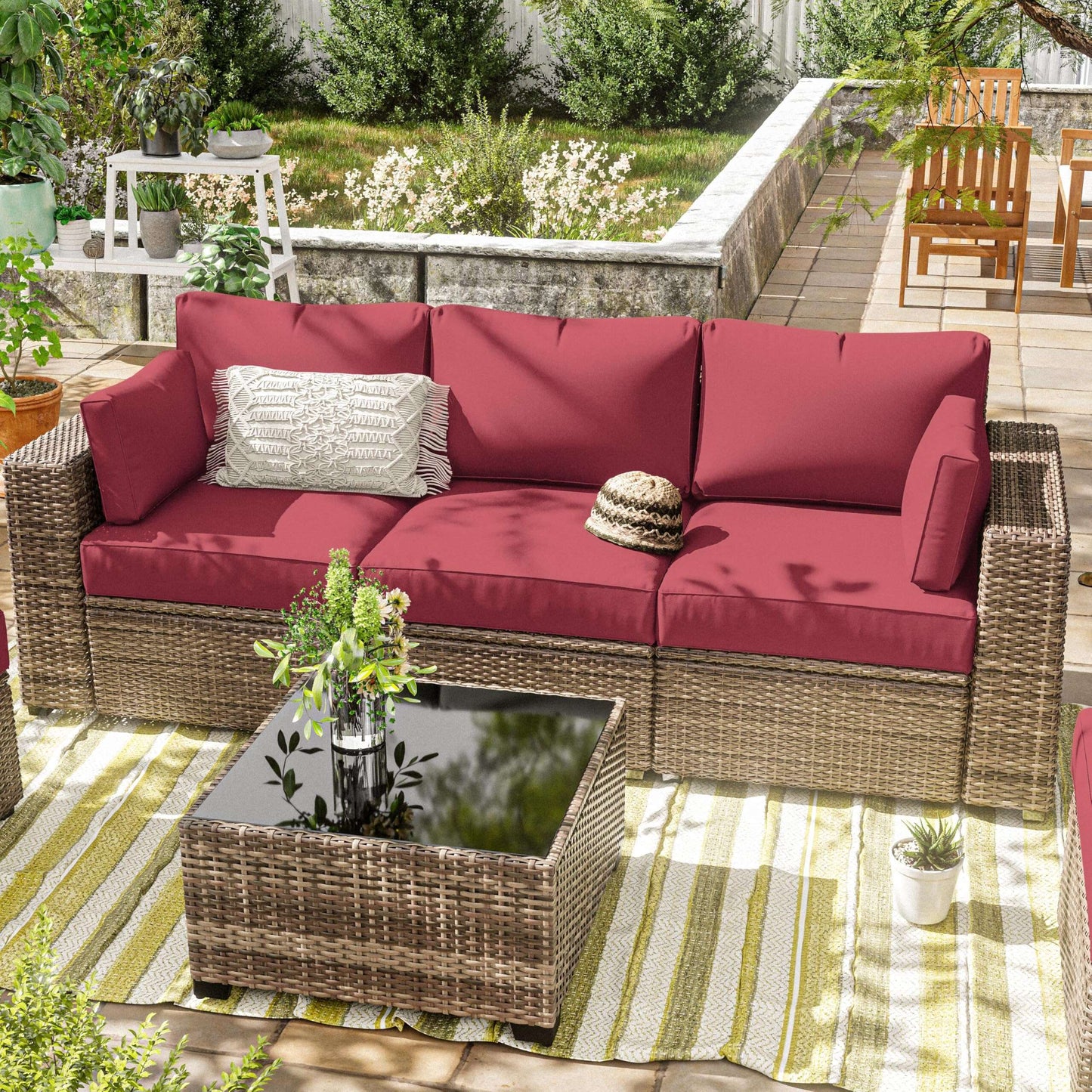 Outdoor wicker patio sofa with fuchsia cushions, decorative pillow, and coffee table on striped rug