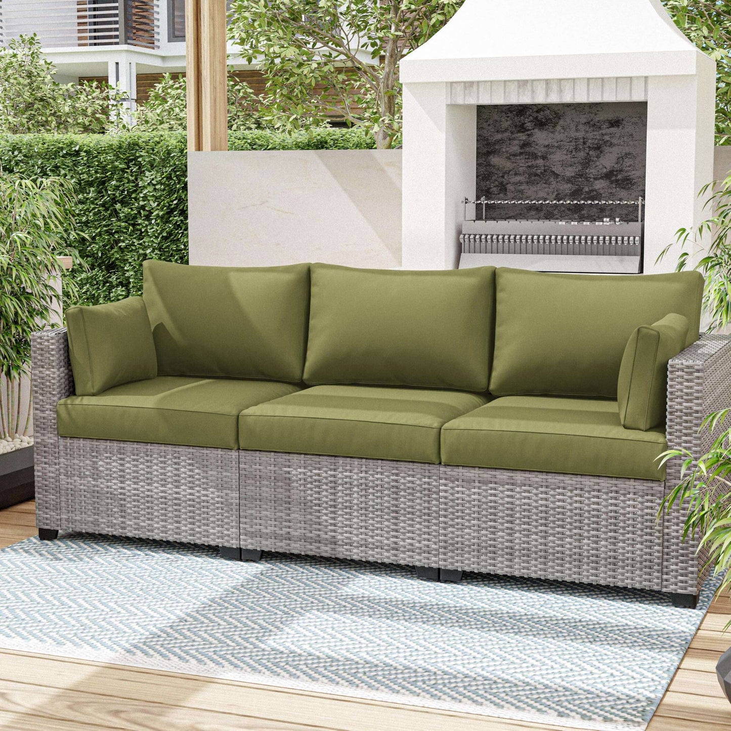 Green cushioned outdoor sofa on a patio with a fireplace and plants in the background