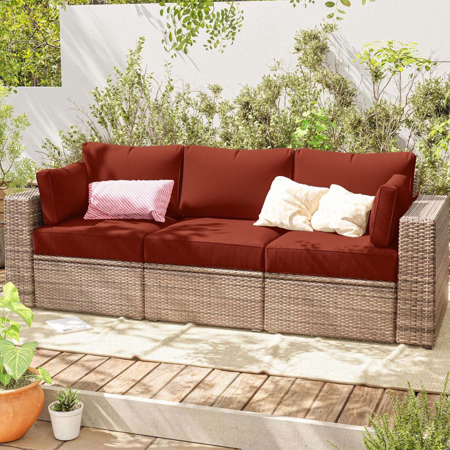 Outdoor sofa with red cushions and decorative pillows on a wooden deck with greenery.