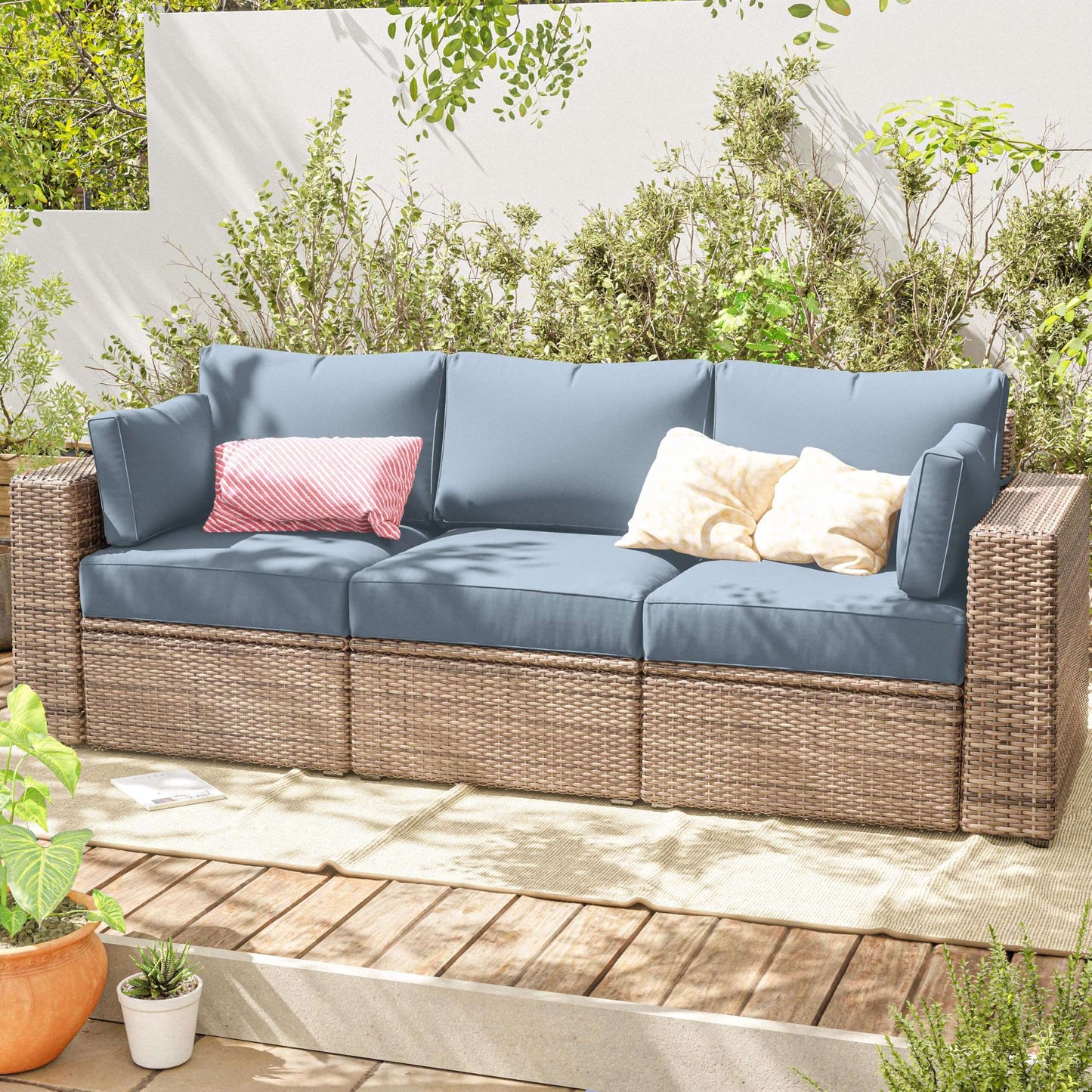 Outdoor sofa with blue cushions and decorative pillows on a wooden deck with greenery.