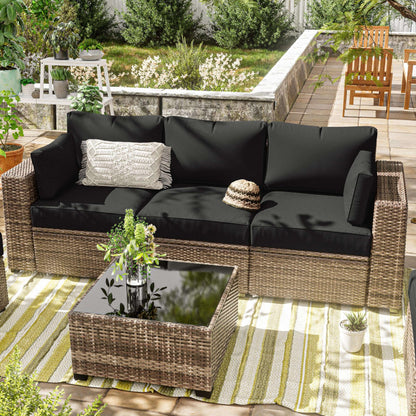 Outdoor rattan sofa with black cushion covers, decorative pillow, and glass-top wicker coffee table on striped rug