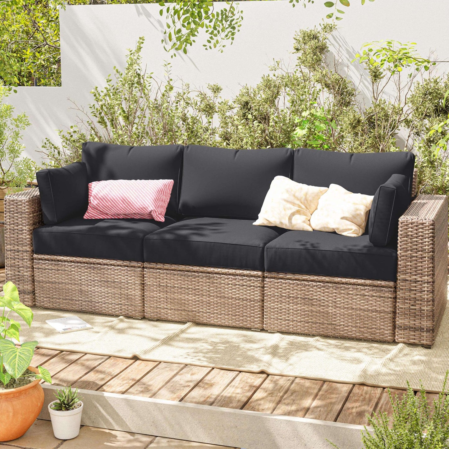 Outdoor sofa with grey cushions and decorative pillows on a wooden deck with plants around.