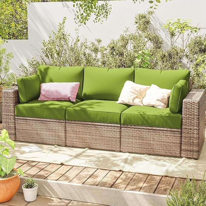Outdoor wicker sofa with green cushions and decorative pillows on wooden deck surrounded by plants