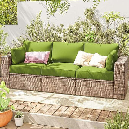 Outdoor wicker sofa with green cushions and decorative pillows on wooden deck surrounded by plants