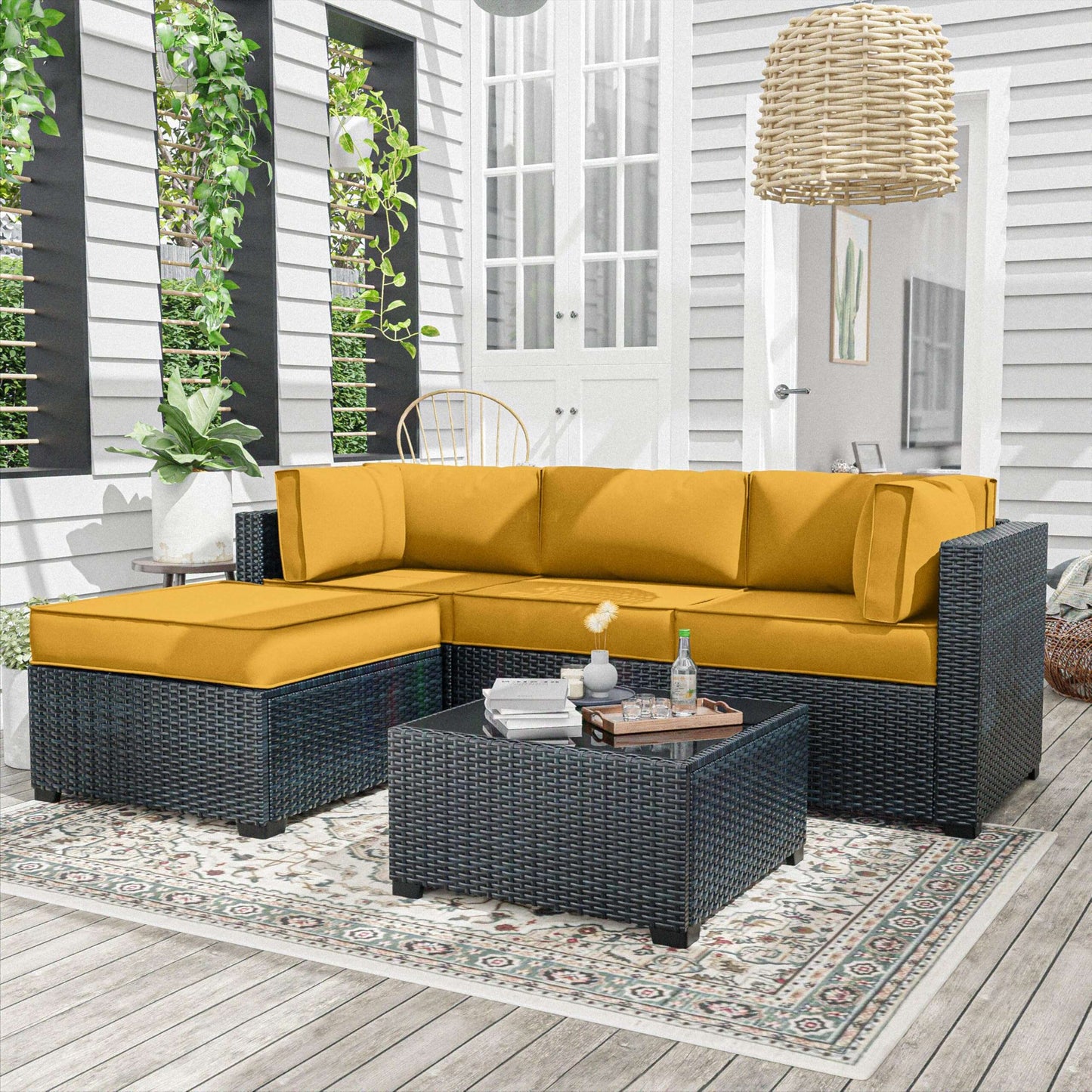 Yellow sectional sofa with dark wicker frames on a wooden deck with plants and a lamp in the background.