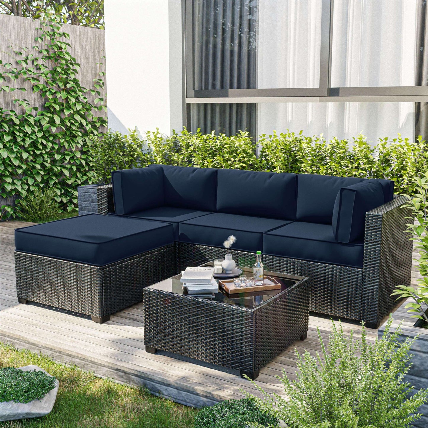 Outdoor patio set with dark blue cushions on wicker sofa and ottoman, glass-top coffee table on wooden deck