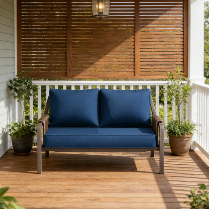 Blue cushioned outdoor sofa on a wooden deck with plants and wooden shutters in the background.