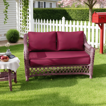 Wicker outdoor sofa with burgundy loveseat cushions on a grassy lawn, white picket fence in the background.