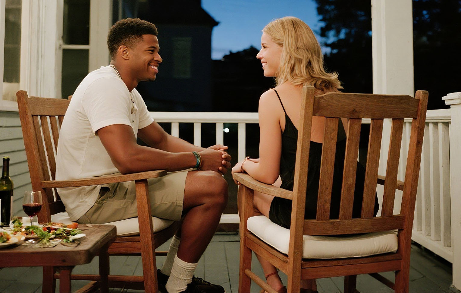 Two people sitting on a porch, engaged in conversation.