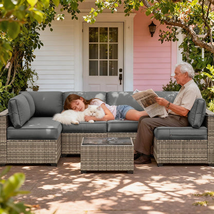 Two people sitting on a gray outdoor sofa with a white dog, reading a newspaper, in front of a pink house.