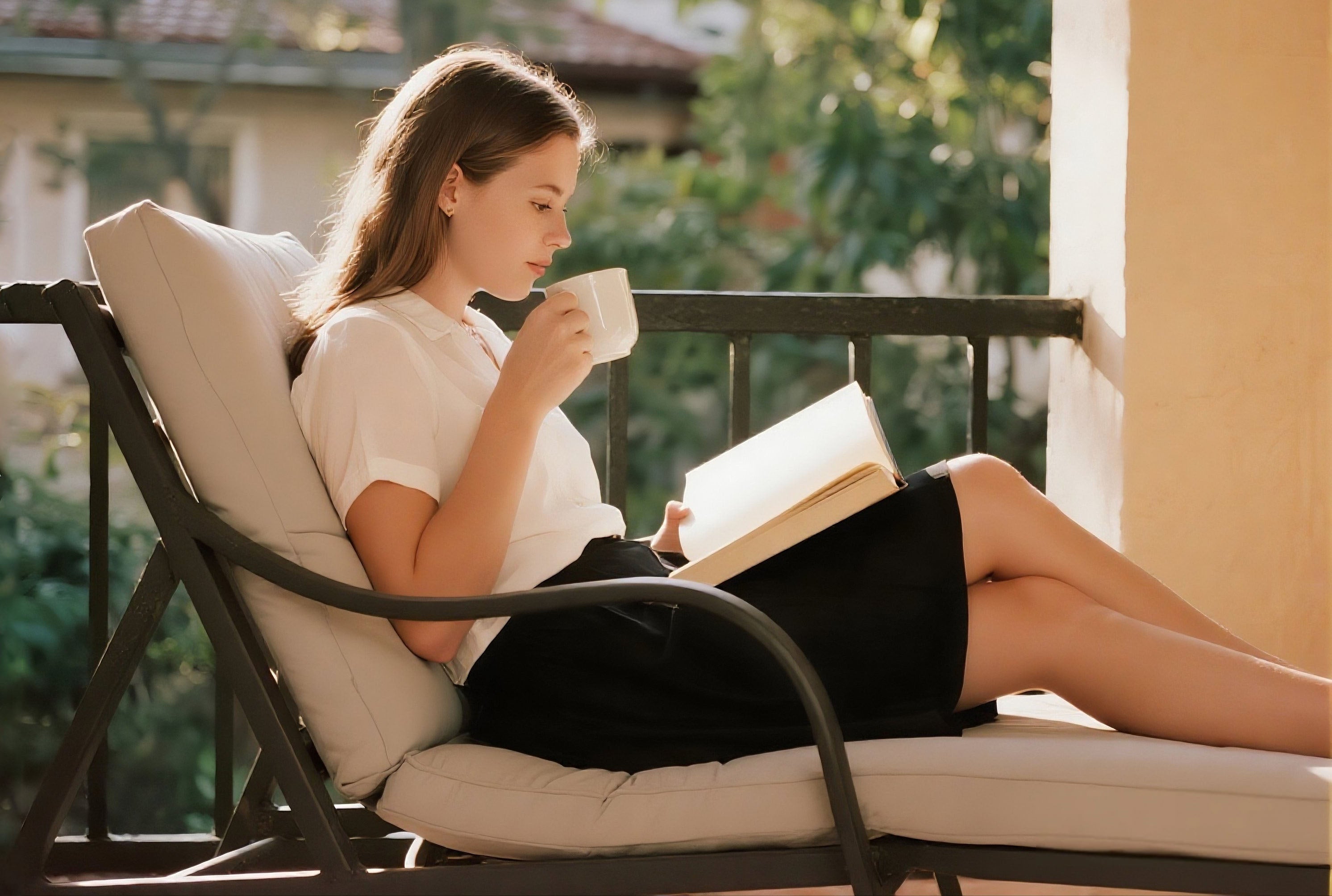 Woman reading a book and drinking from a cup on a balcony