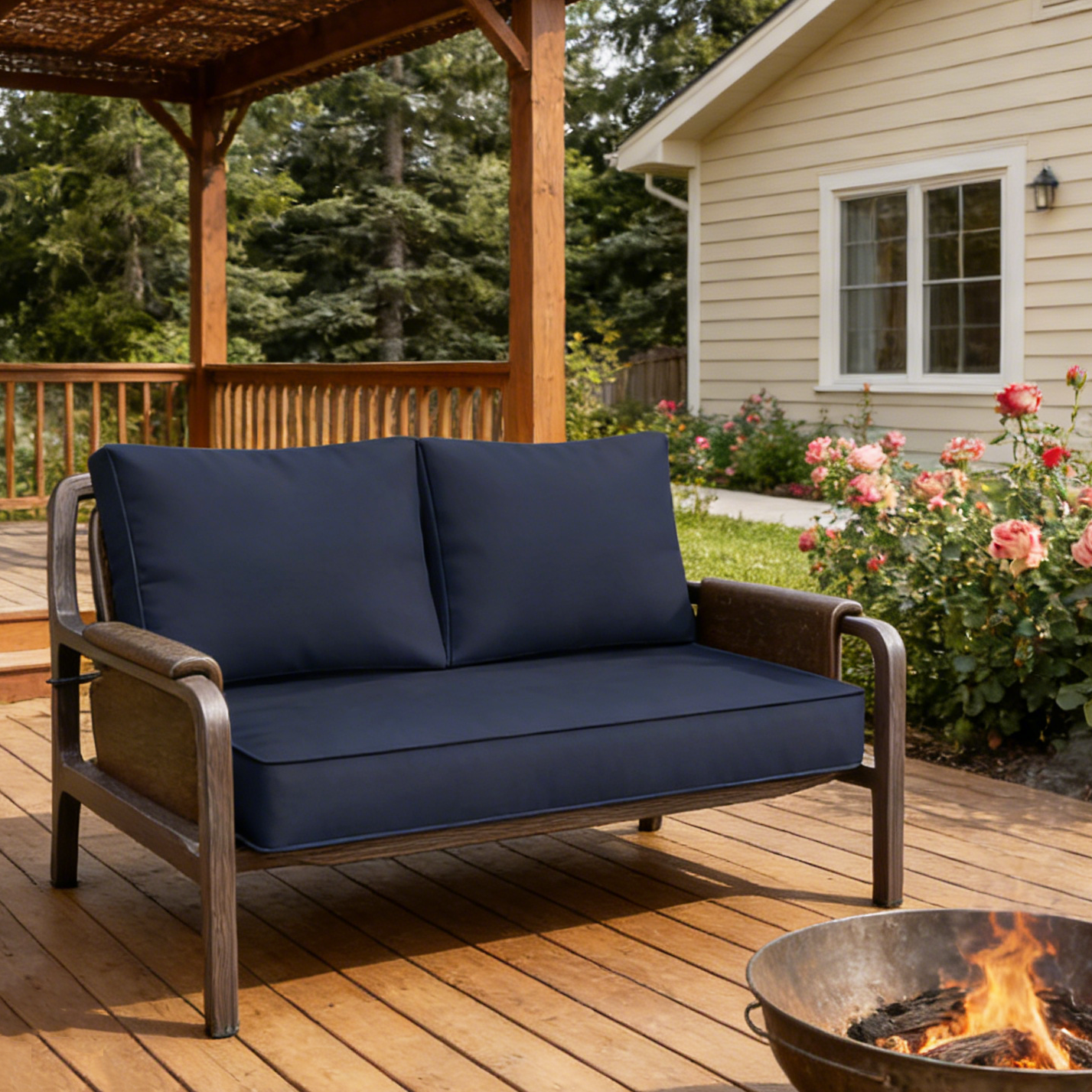 Navy blue cushioned outdoor loveseat on a wooden deck with a fire pit and house in the background.