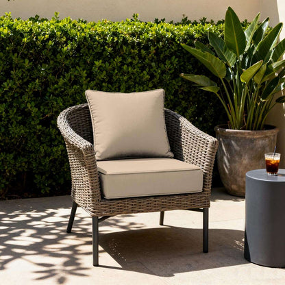 Wicker chair with beige cushions in an outdoor setting with plants and a drink.