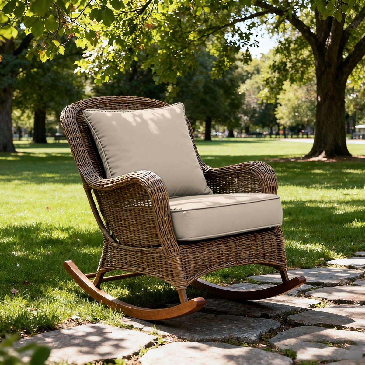 Wicker rocking chair with beige cushions on a stone path in a park.