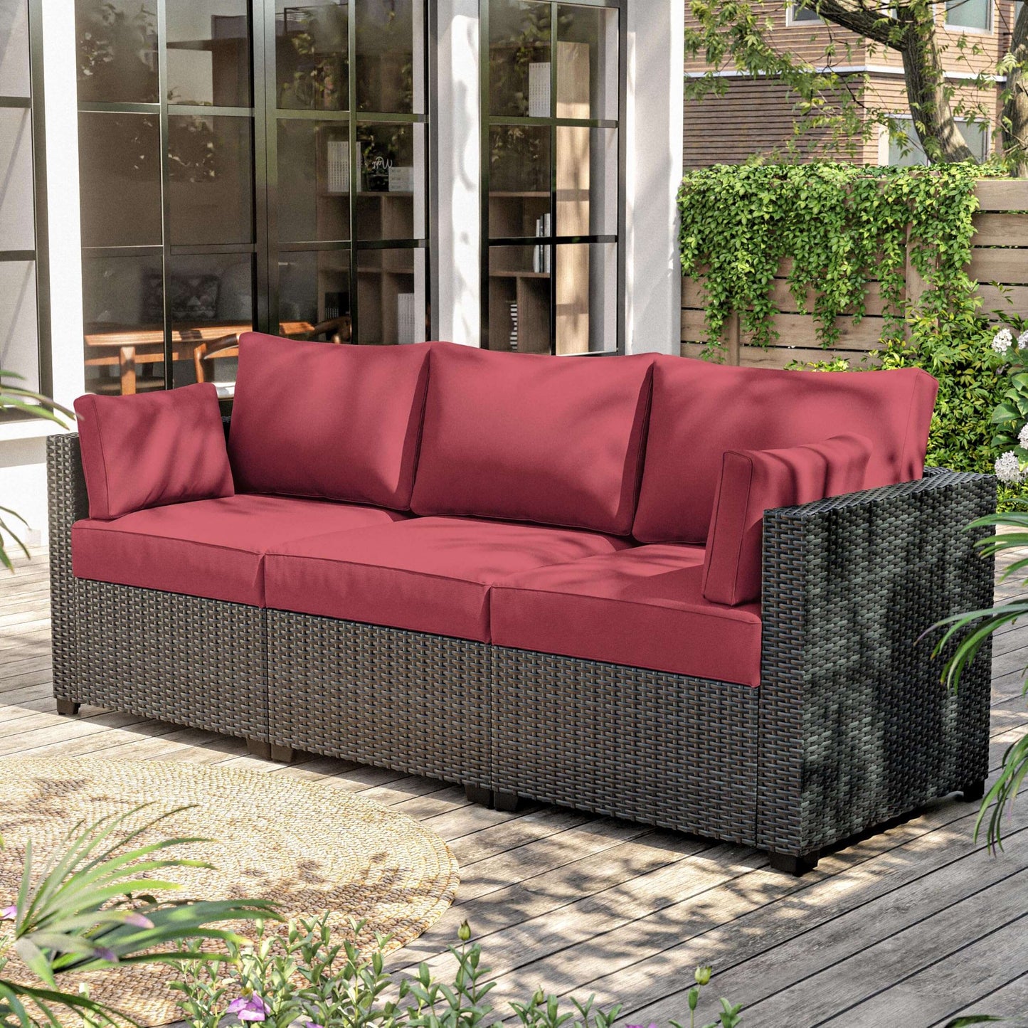 Modern outdoor wicker patio sofa with deep red cushions on wooden deck surrounded by greenery