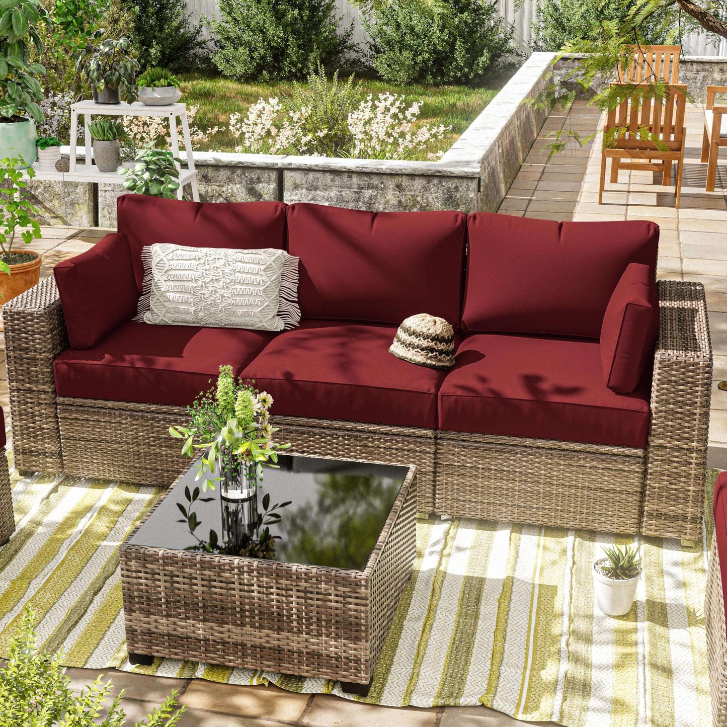Outdoor patio set with burgundy cushions and a glass table on a striped rug.