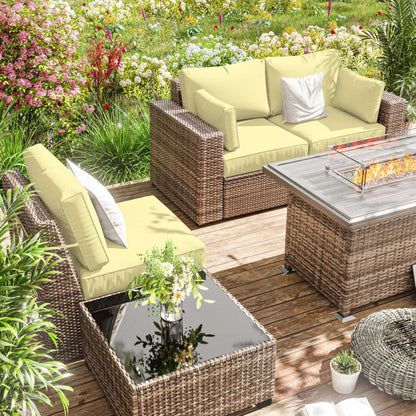 Outdoor patio with yellow cushioned rattan sofas, glass-top coffee table, fire pit, and vibrant garden