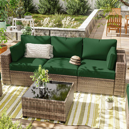 Outdoor rattan sofa with olive green cushions, decorative pillow, and glass-top wicker coffee table on striped rug