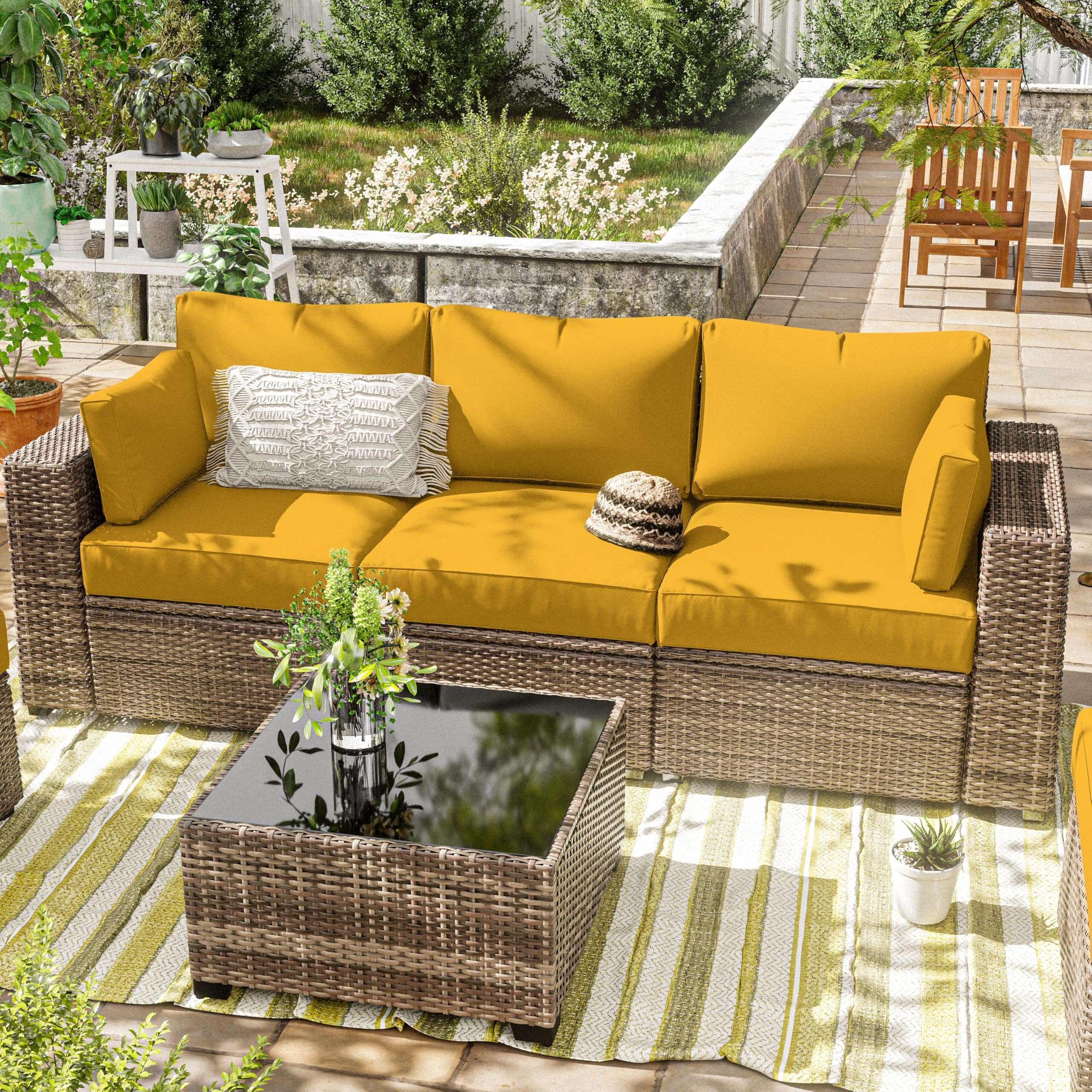 Outdoor patio with wicker sofa featuring mustard yellow cushions, a coffee table, and potted plants