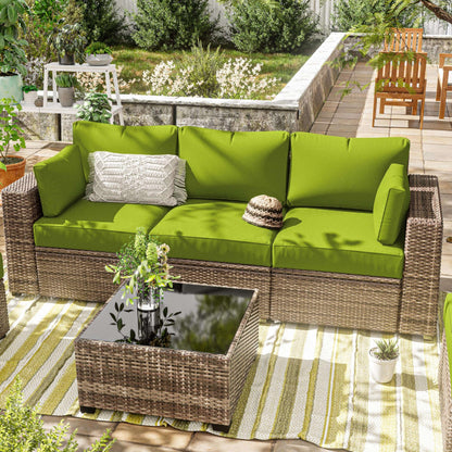 Outdoor patio with wicker sofa featuring grass green cushions, decorative pillow, and glass-top coffee table